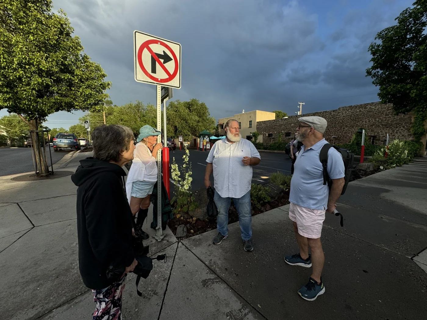 Guests gather with their guide at a Southside Flagstaff street corner as evening light breaks through storm clouds over the old stone buildings