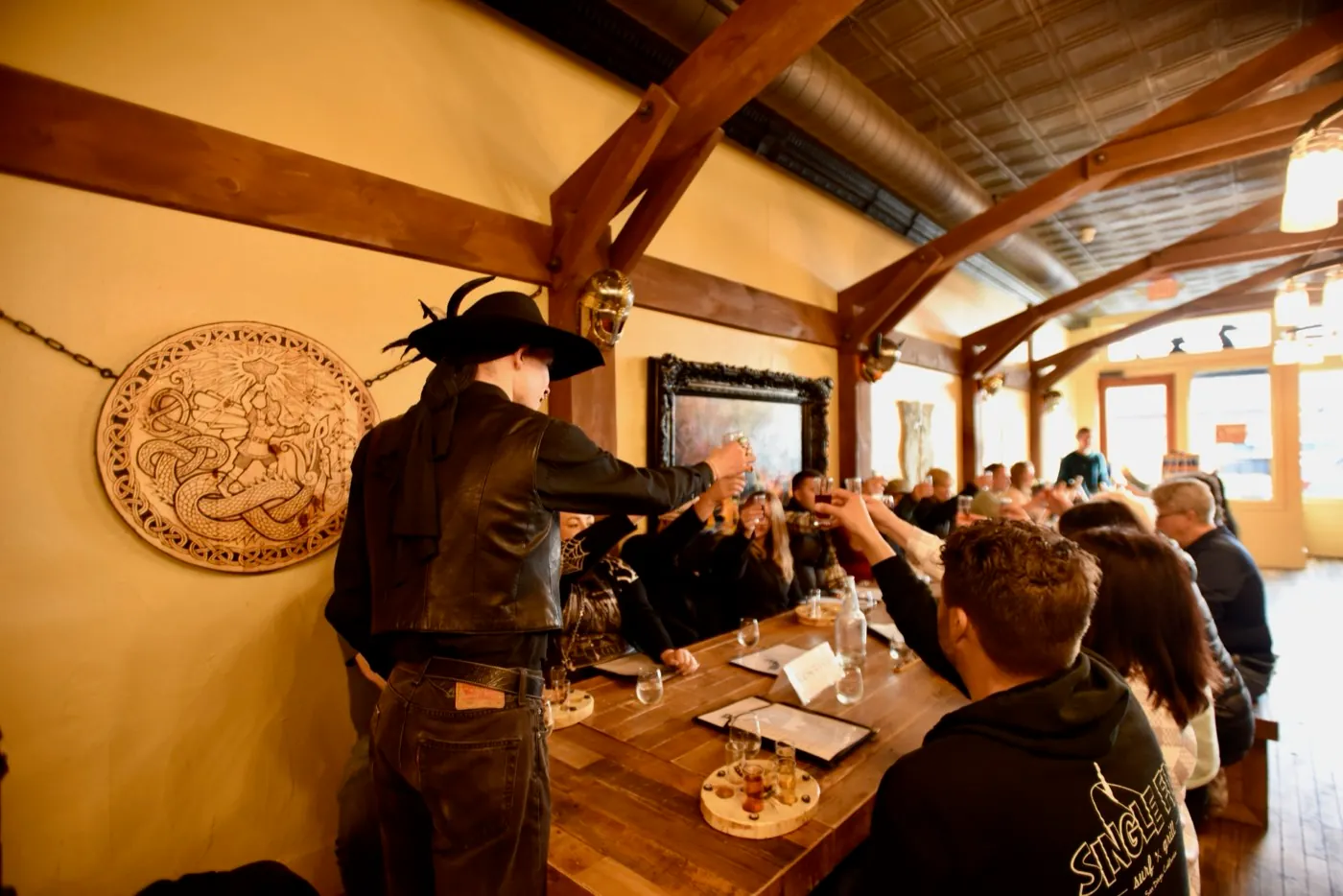 A Freaky Foot Tours guide in a black hat and leather raises a toast and the whole table follows at a Spirits With The Spirits pub crawl stop