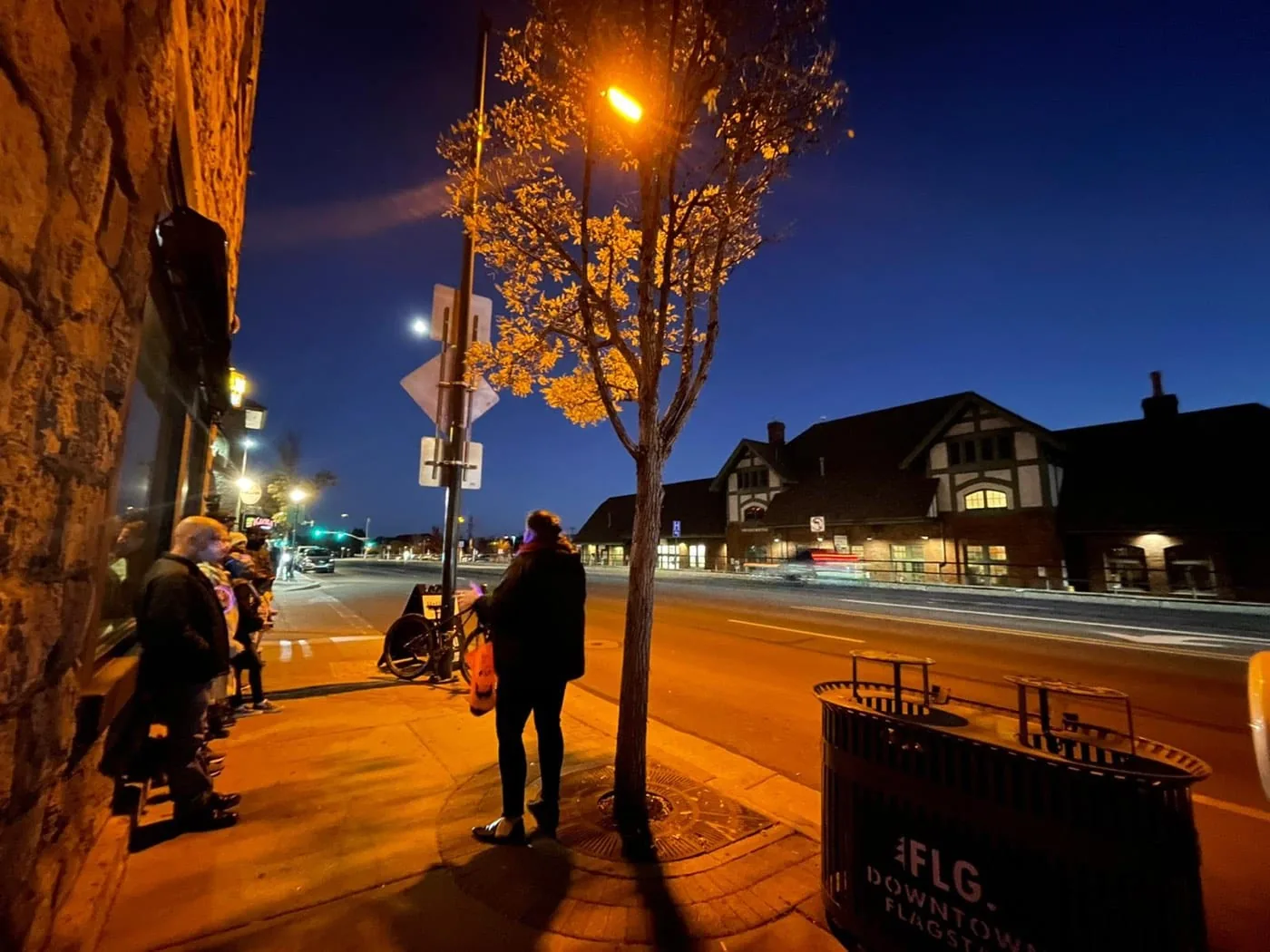 A Freaky Foot Tours group on a dark Flagstaff sidewalk at night with the train depot lights in view
